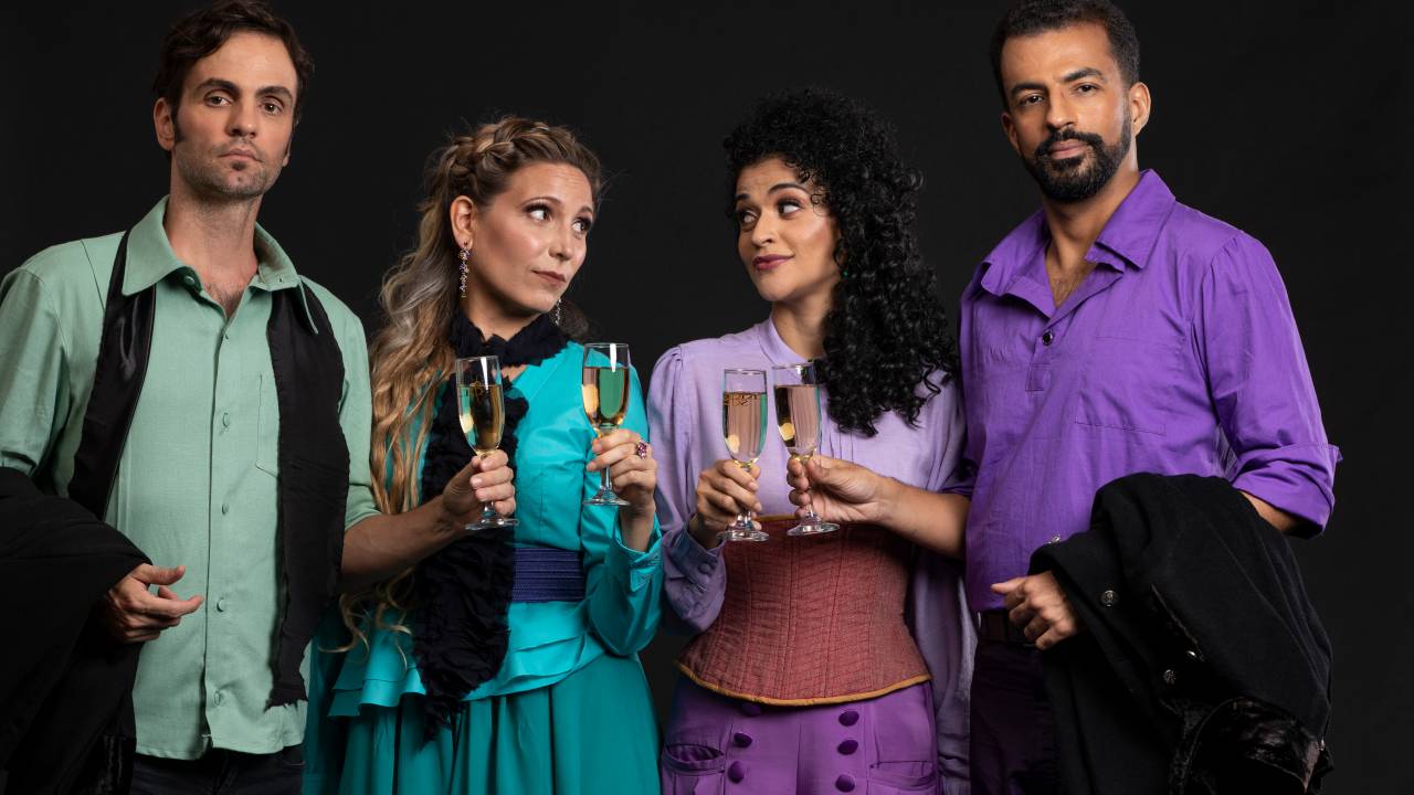 Imagem mostra quatro pessoas com roupas de gala coloridas, brindando copos