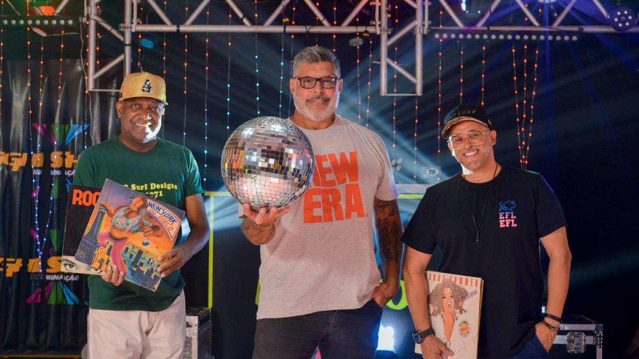 Imagem mostra três homens sorrindo, com globos espelhados e discos de vinil