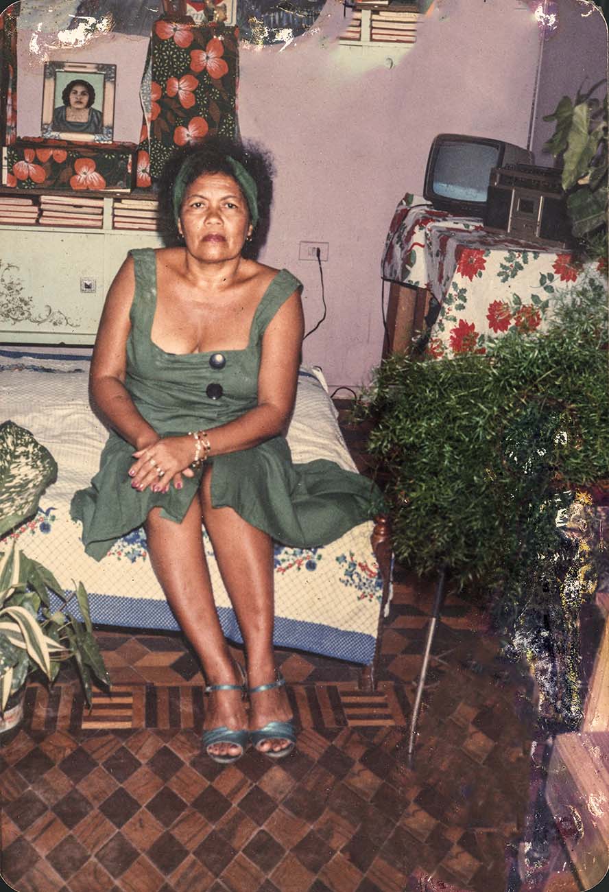 Imagem mostra mulher sentada em cama, dentro de quarto