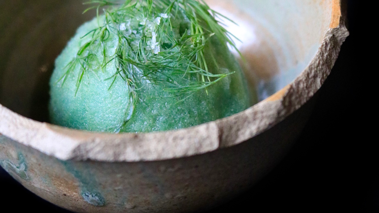Cumbuca de cerâmica com bola de sorvete verde água e ervas frescas por cima