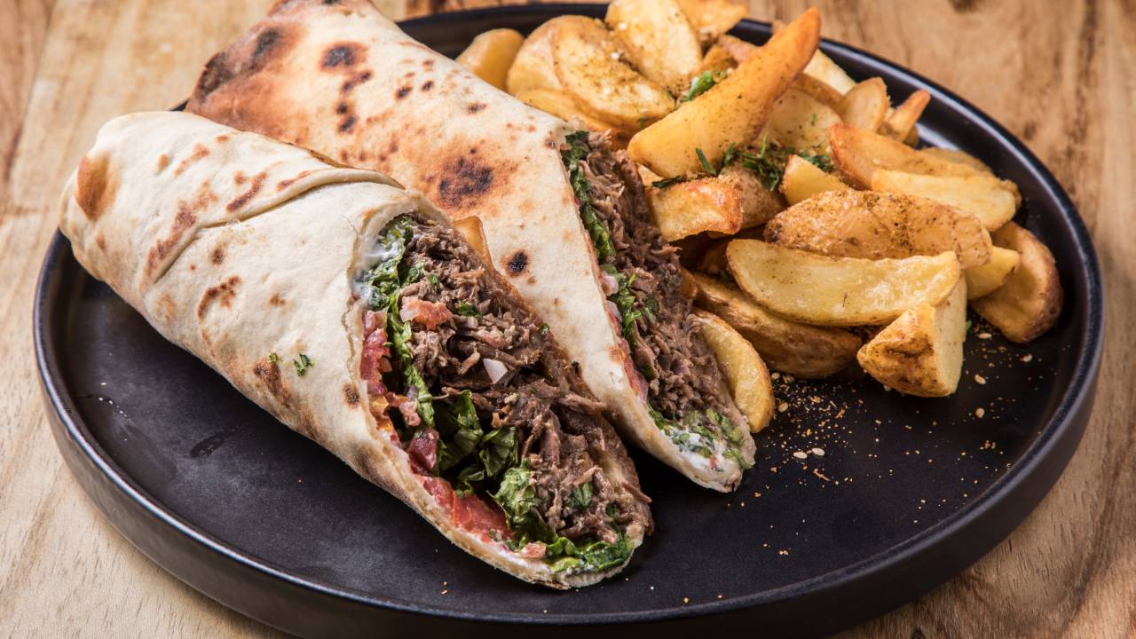 Shawarma de cordeiro cortado em 2 metades acompanhado de batata frita sobre prato de cerâmica