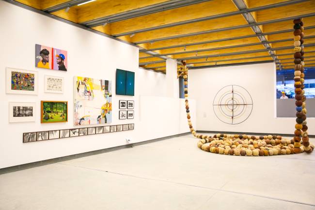 Sala branca com exposição artística: quadros na parede da esquerda e diversas bolas empilhadas no canto direito