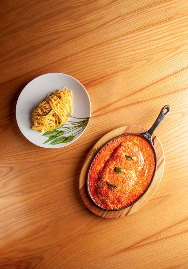 Filé alla parmegiana com tagliolini _5.jpg Parmigiana em panela de ferro sobre tábua ao lado de prato de porcelana com tagliolini na manteiga de sálvia