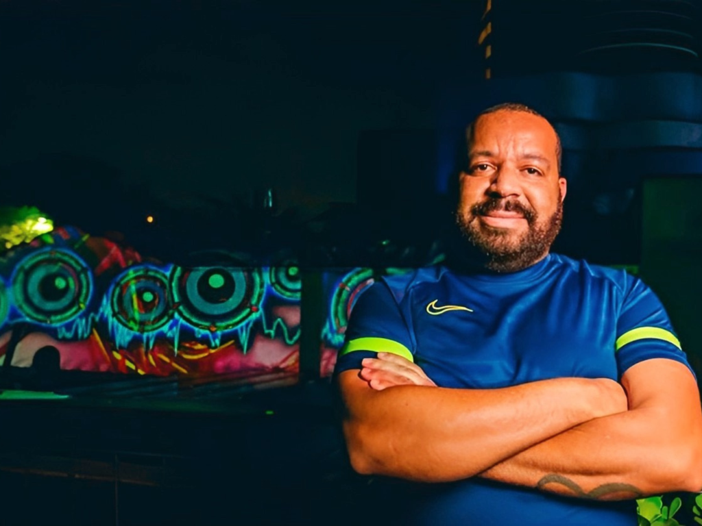 VJ Mole Imagem mostra homem com a camisa do Brasil de braços cruzados. Ao fundo, projeções em um prédio