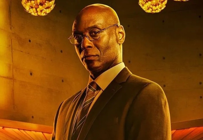 Foto de Lance Reddick em fundo neutro, usando terno, com filtro sepia