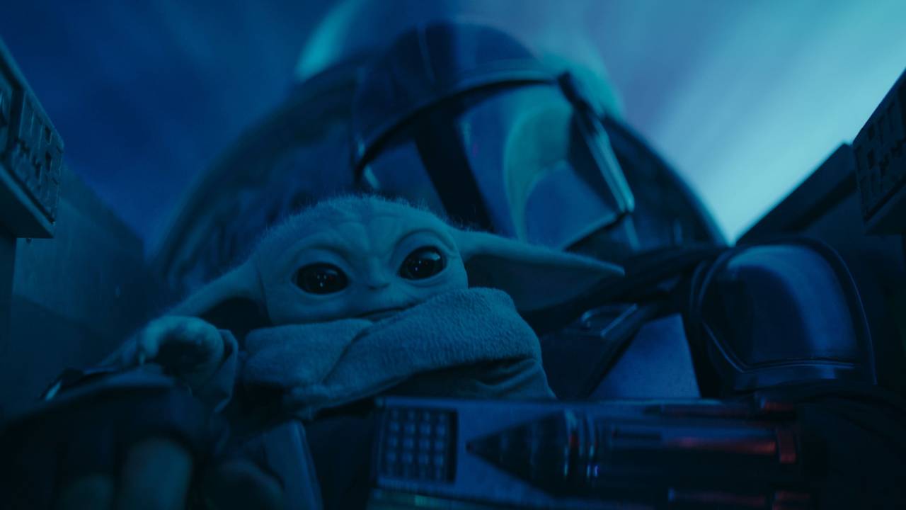 Homem com capacete prata e Baby Yoda juntos em nave
