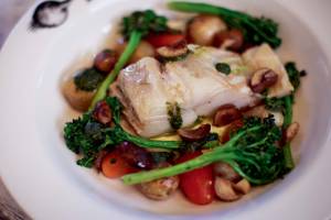 manioca lombo de bacalhau Prato de porcelana branca contendo lombo de bacalhau, brócolis, chalota, tomate cereja e batatas tostadas e vinagrete verde de castanha portuguesa