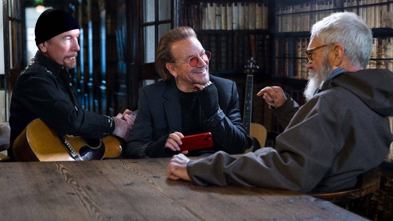 Três homens conversam em uma biblioteca, sorrindo