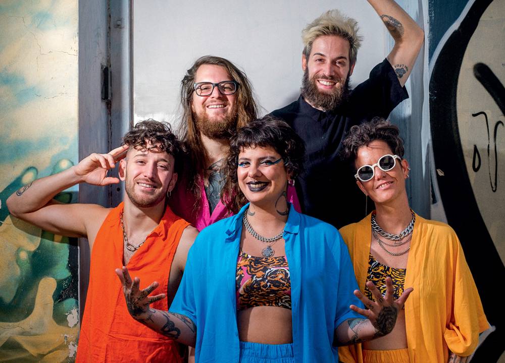 Imagem mostra cinco pessoas sorrindo e vestindo roupas coloridas