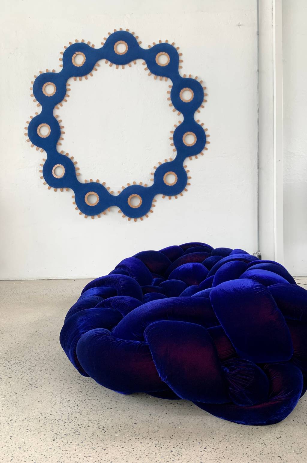 Poltrona com formato de pufe na cor azul-esuro e adorno circular na parede ao fundo.
