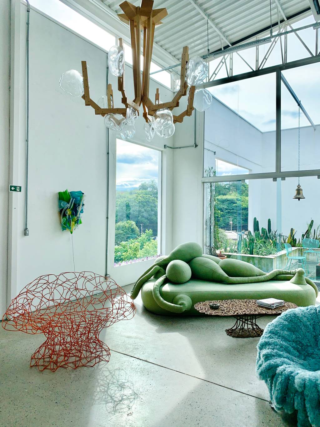Espaço com janelas e teto de vidro adornados por sofá verde e peças de arte.