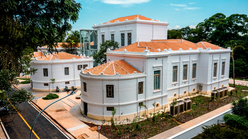 Fachada central do Edifício Vital Brazil, com paredes brancas, jardim na frente e telhado marrom.