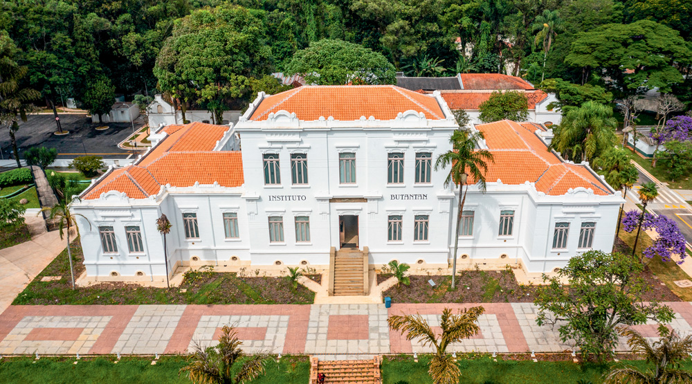 Fachada central do Edifício Vital Brazil, com paredes brancas, jardim na frente e telhado marrom.