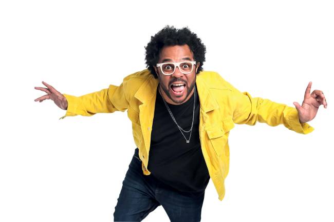 Marcelo Marrom Homem negro de óculos com blusa amarela de braços abertos