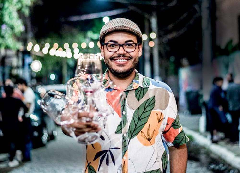 Homem pardo de camisa florida e boina bege, com barba, bigode e óculos