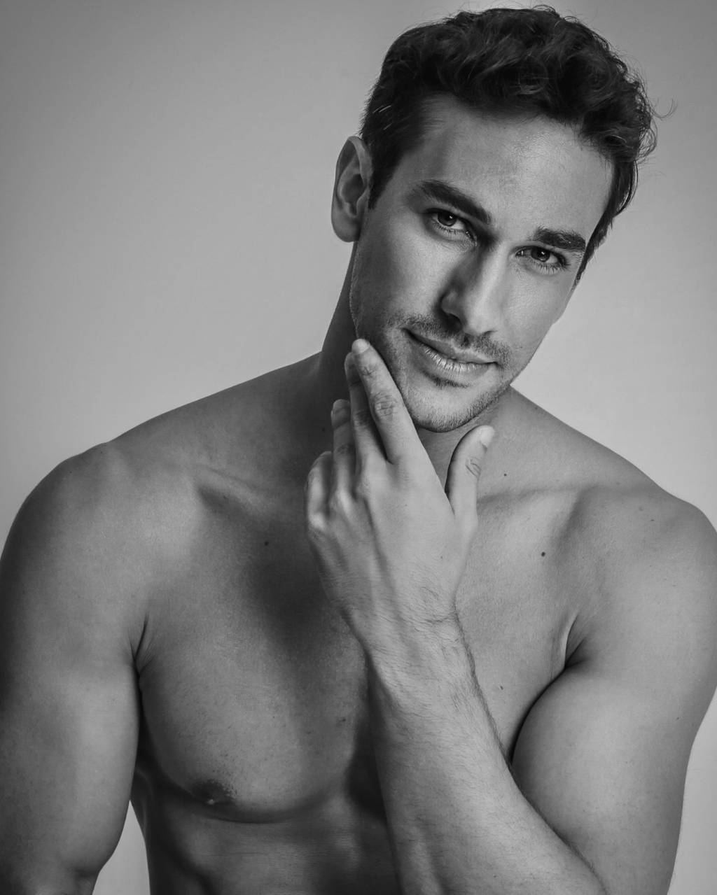 Henrique Martins (Raffa Rodrigues-Divulgação) Homem musculoso sem camisa apoia uma das mãos no queixo e encara a câmera com meio sorriso. A imagem está em preto e branco.