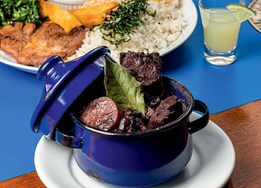Feijoada em panela de ferro esmaltado com acompanhamentos em prato de porcelana