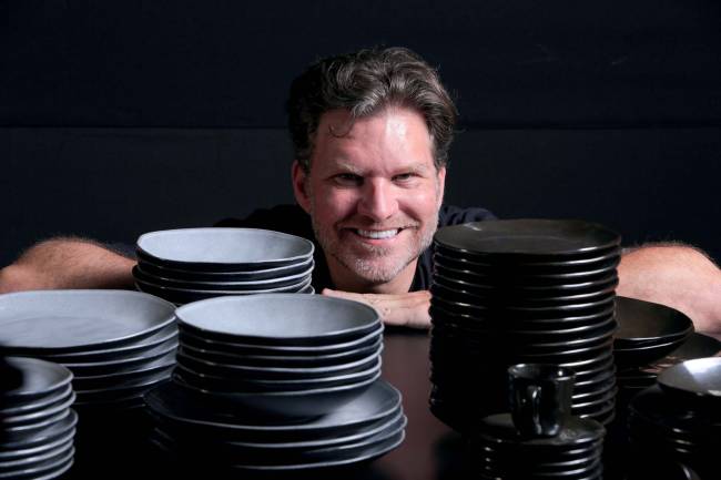 Homem debruçado em mesa com pilhas de pratos nos dois lados