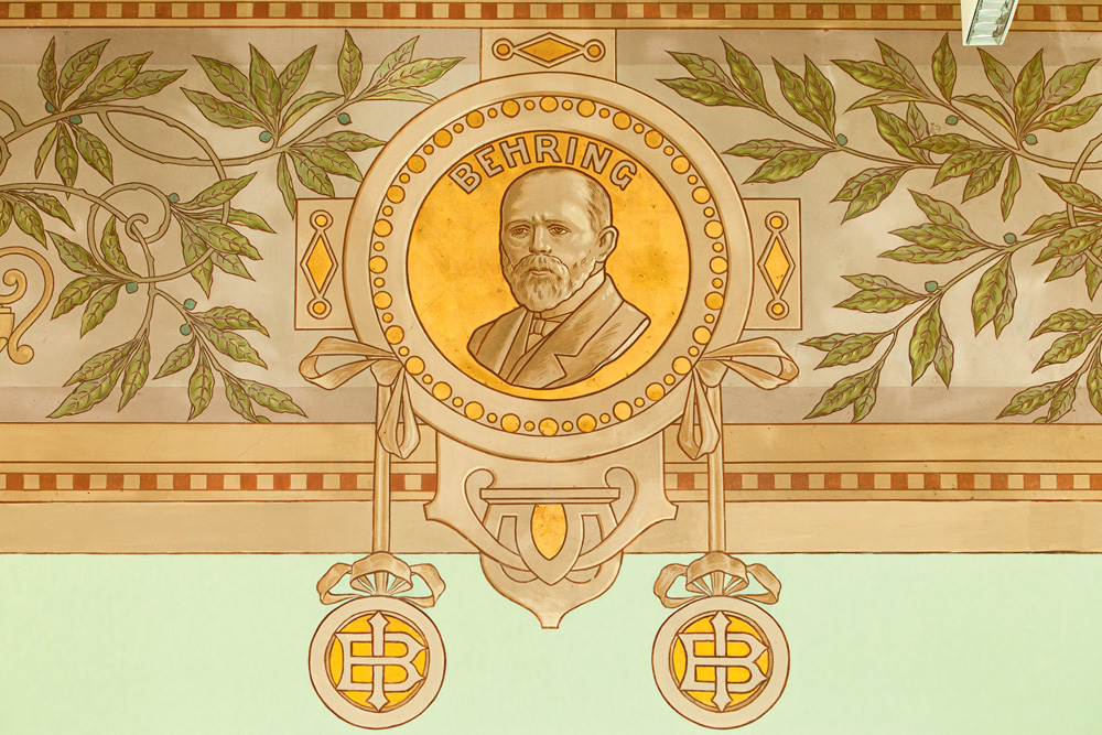 Imagem de afresco restaurado em cores douradas e busto de homem calvo no centro.