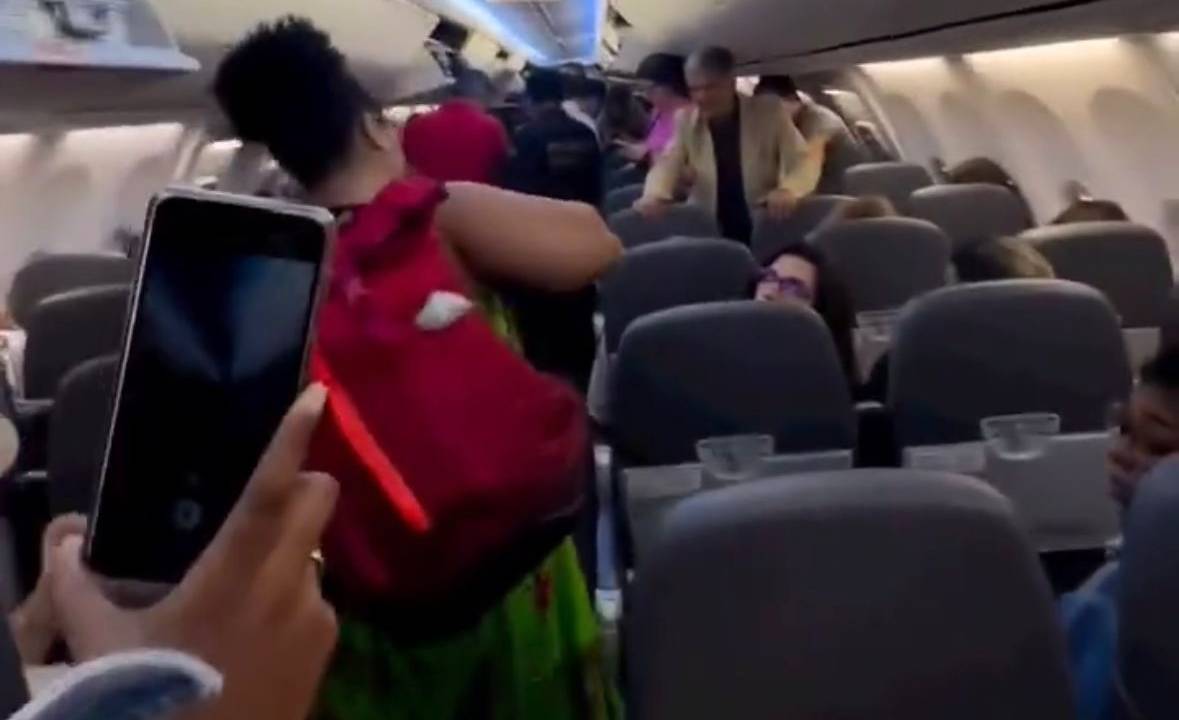 Mulher com mochila vermelha nas costas anda por corredor de avião