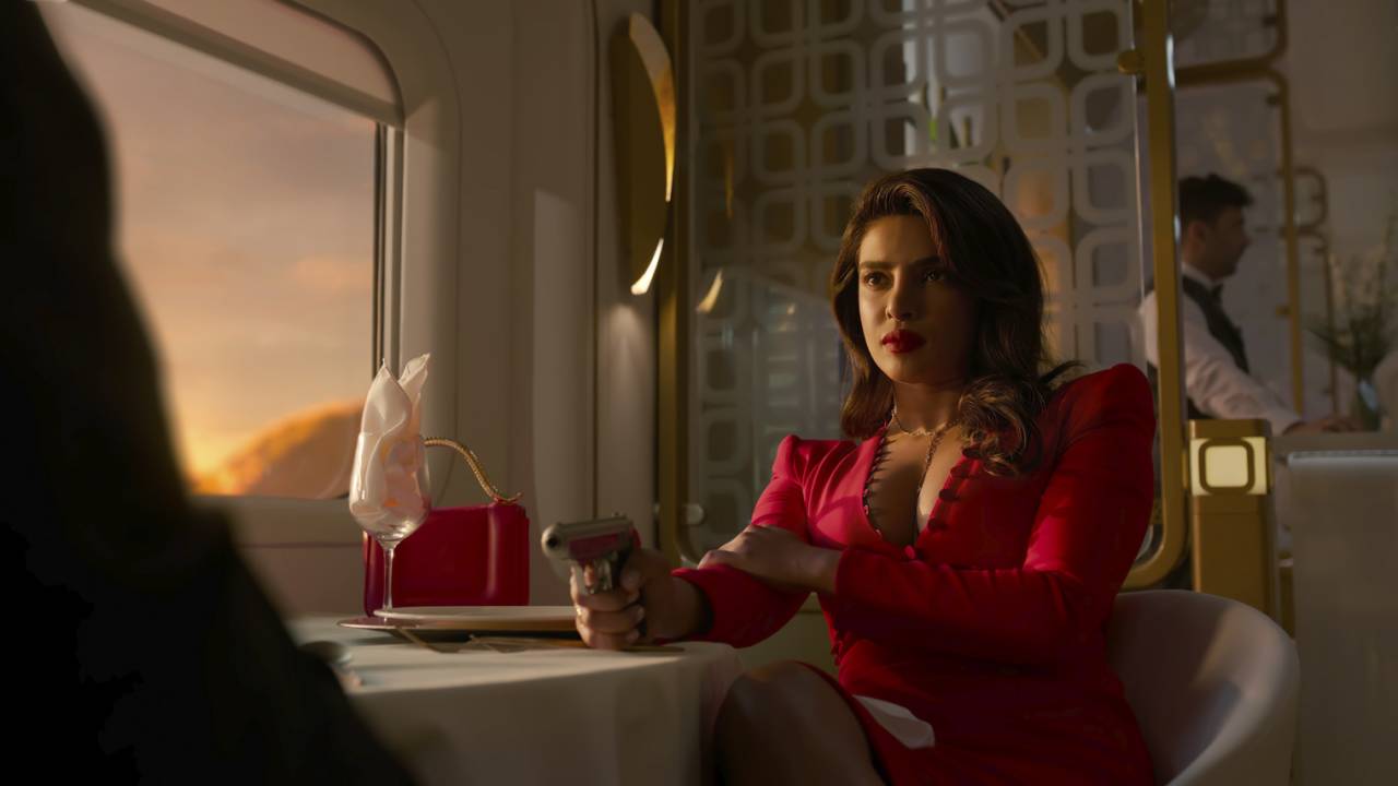 Priyanka Chopra, de vestido vermelho, aponta arma para homem fora da imagem