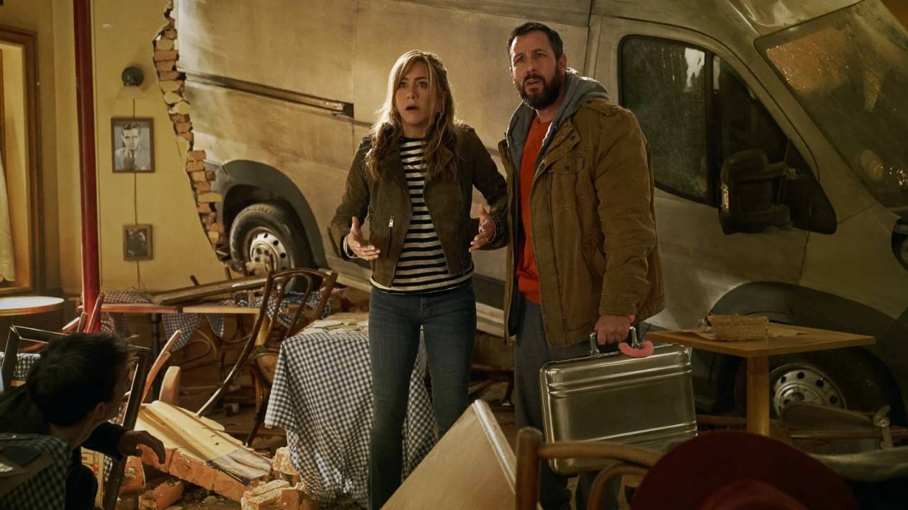 Jennifer Aniston e Adam Sandler pasmos na frente de uma van destruída