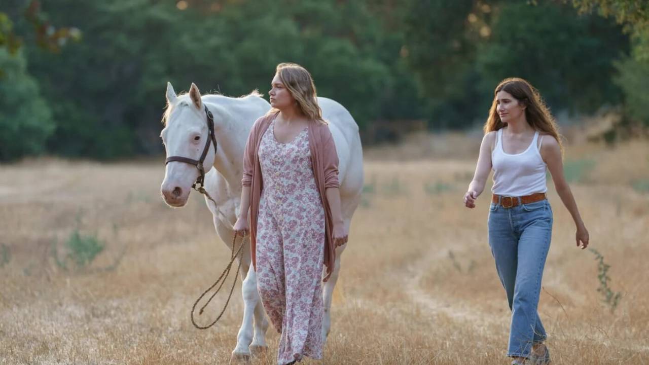 Duas mulheres e um cavalo branco andam pelo campo