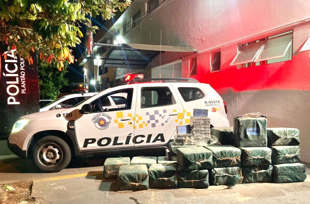 pacotes de cocaína e viaturas da polícia militar ao fundo