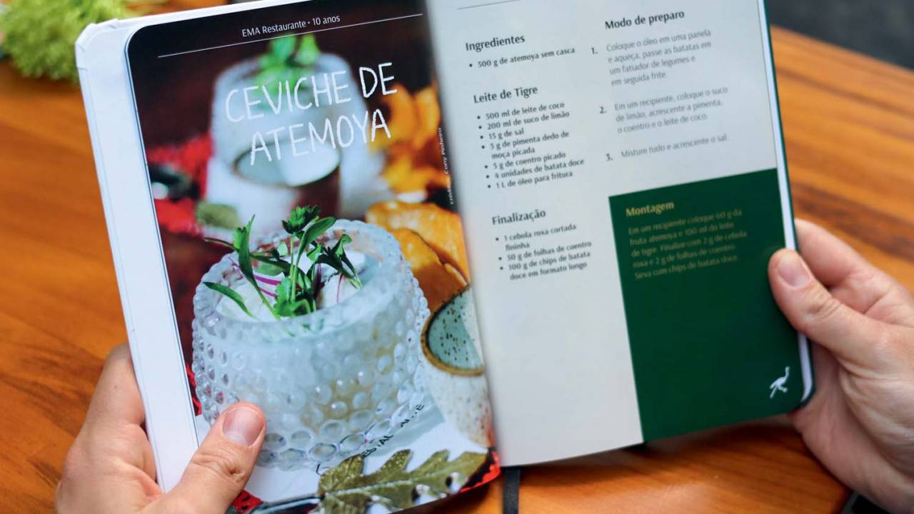 Mãos segurando livro aberto em páginas de receita de ceviche de atemoia.