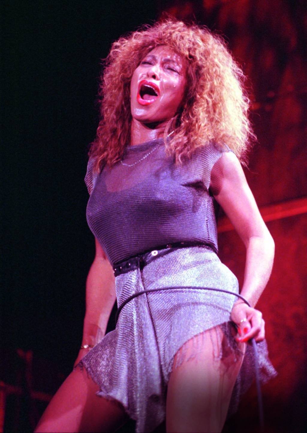 Imagem mostra mulher em palco, com roupa brilhante e a boca aberta