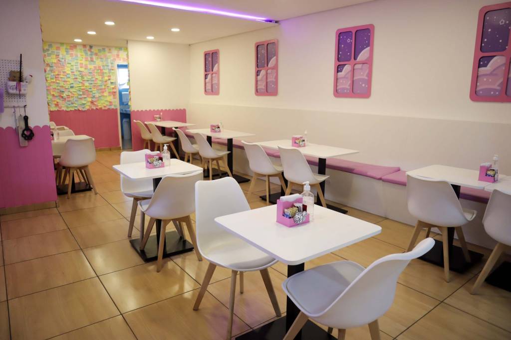 Salão de cafeteria com paredes, mesas e cadeiras brancas e detalhes em rosa.