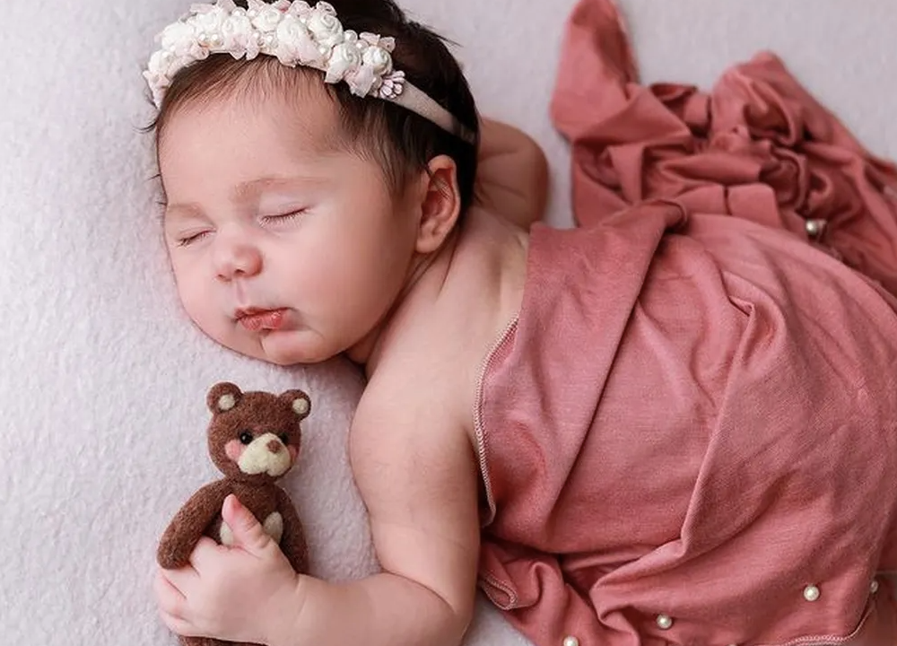 Uma bebê dormindo com um ursinho na mão