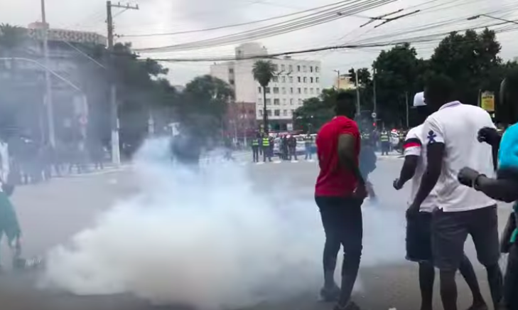 Homens se movimentam entre uma fumaça emitida por bomba de gás