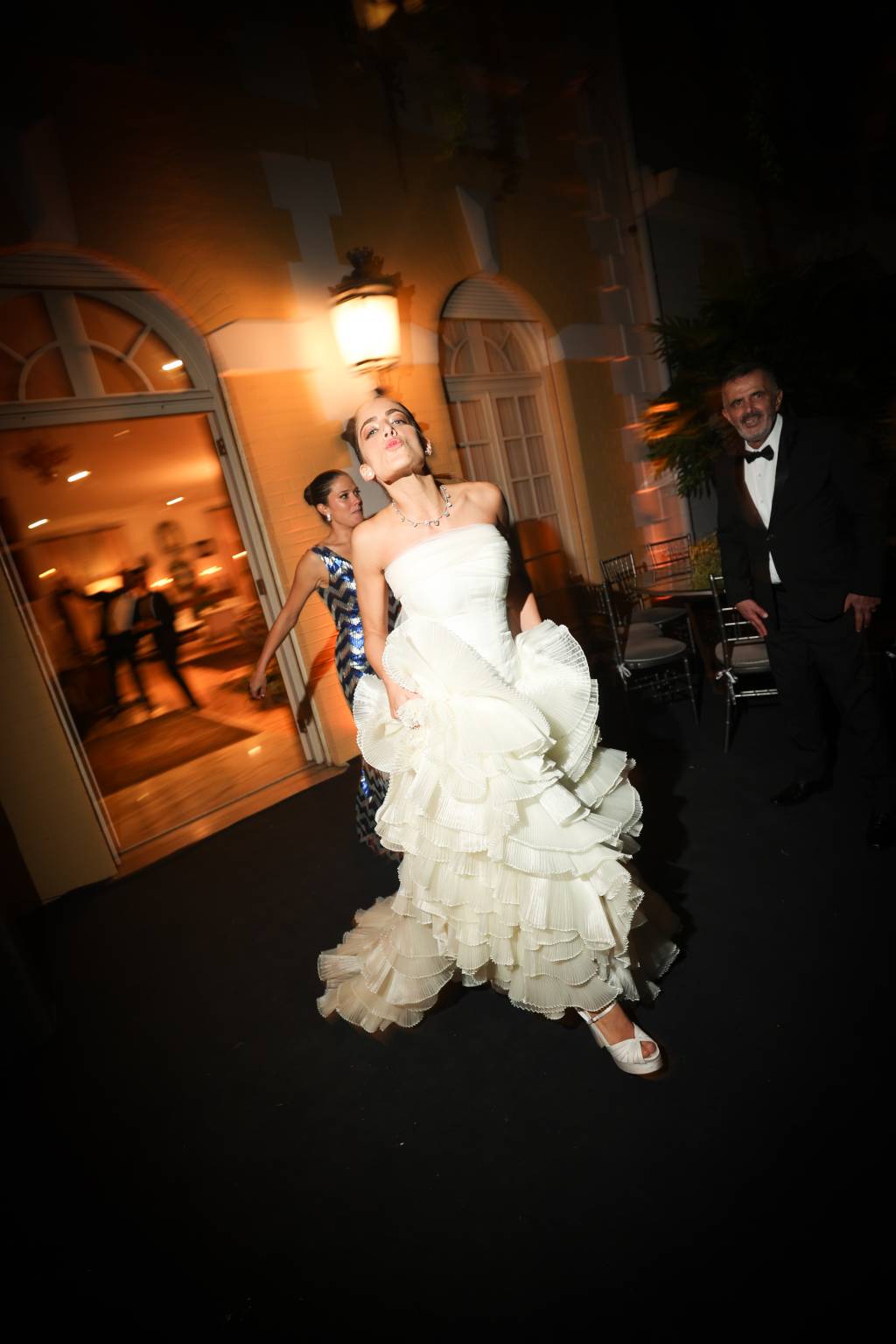 Foto em ambiente externo escuro mostra noiva caminhando com o queixo levantado e as mãos segurando a cauda do vestido branco.