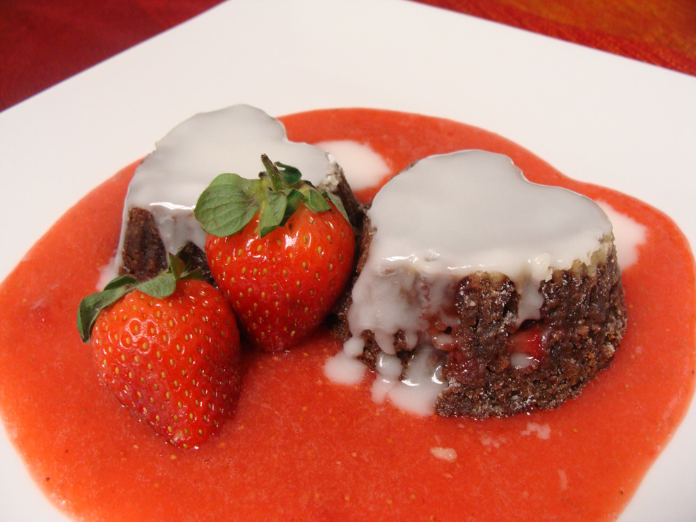 Sobremesa de chocolate em forma de coração sobre calda vermelha e morangos.