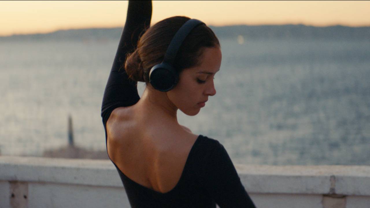 Jovem dança ballet na praia com fone de ouvido