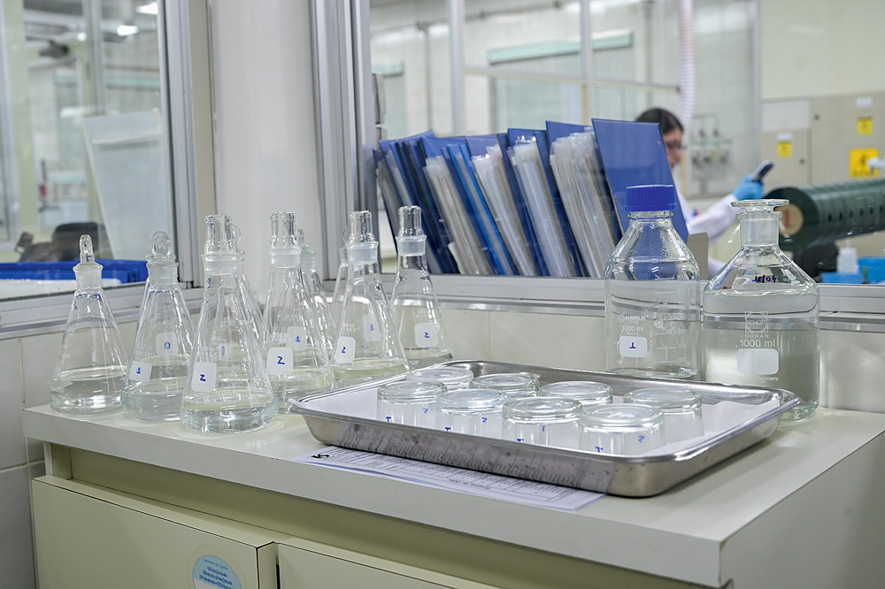 Bancada de laboratório com frascos erlenmeyer lado a lado e bandeja de alumínio com potinhos de vidro.