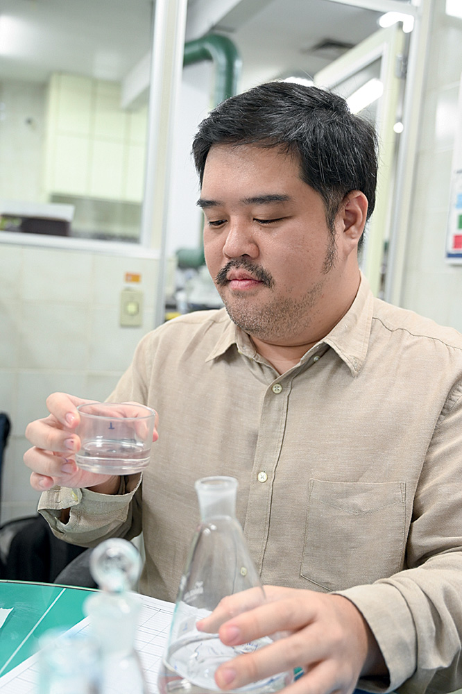 Homem asiático de camisa social segurando erlenmeyer e potinho de vidro com água.