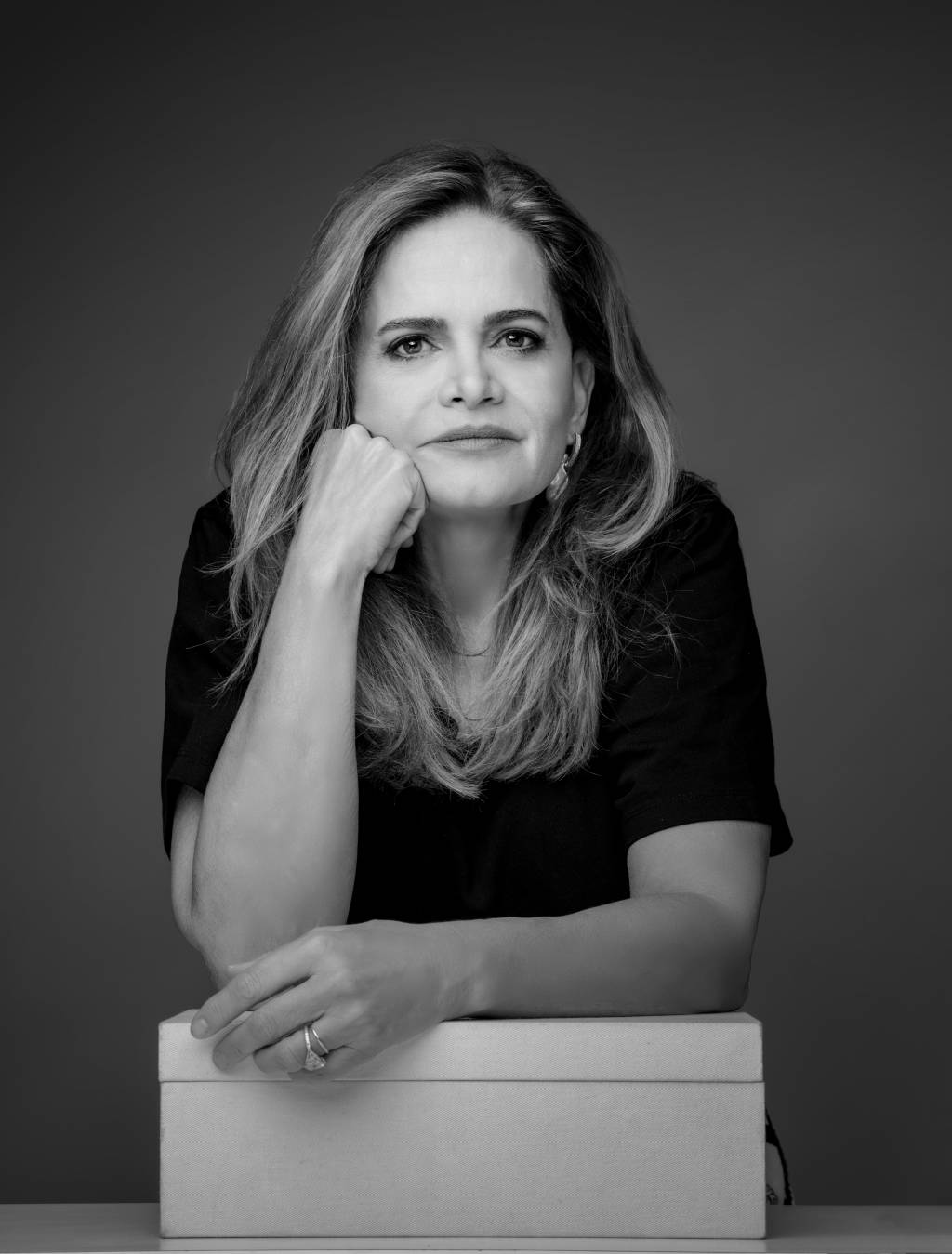 Denise Cassou (Brasilio Wille-Divulgação) Mulher branca posa com uma mão no queixo e a outra apoiada em caixa branca.