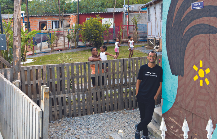 Imagem mostra homem apoiado em muro grafitado, com mulher e crianças no quintal ao lado