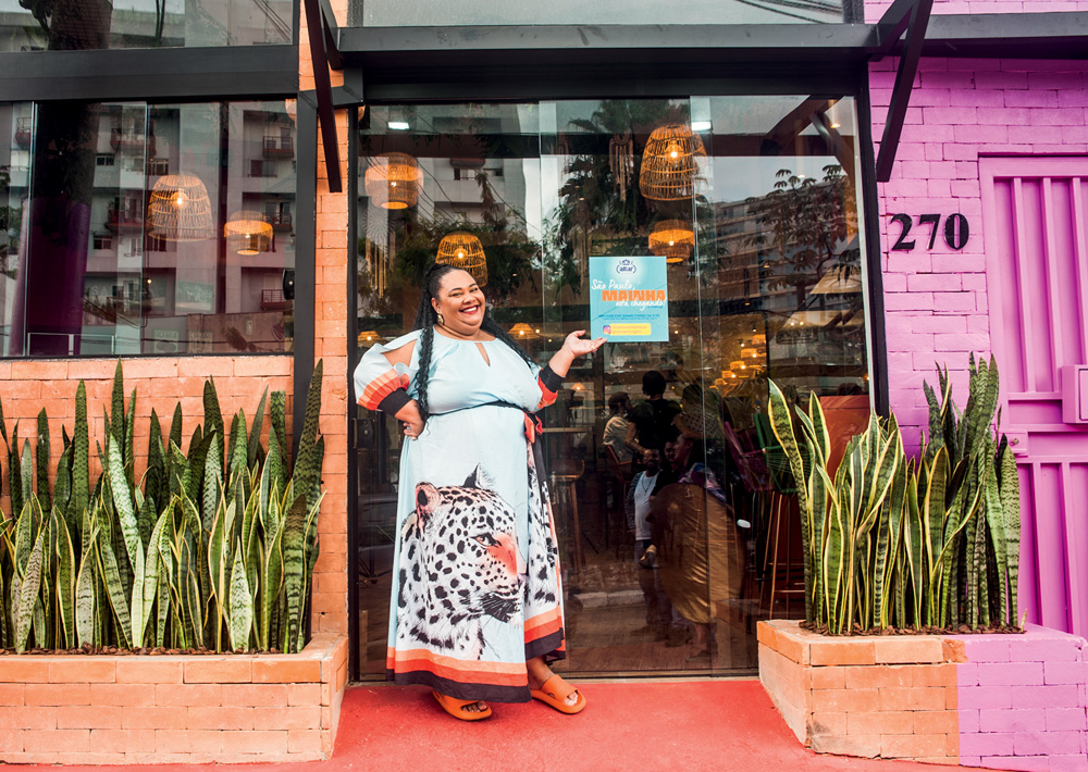 Mulher de vestido colorido em frente a fachada de restaurante.