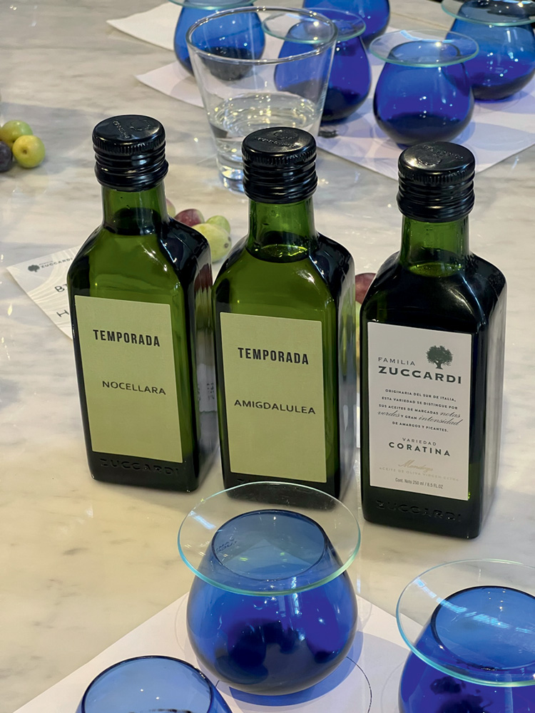 Três garrafas verdes de azeite lado a lado junto e taças azuis.