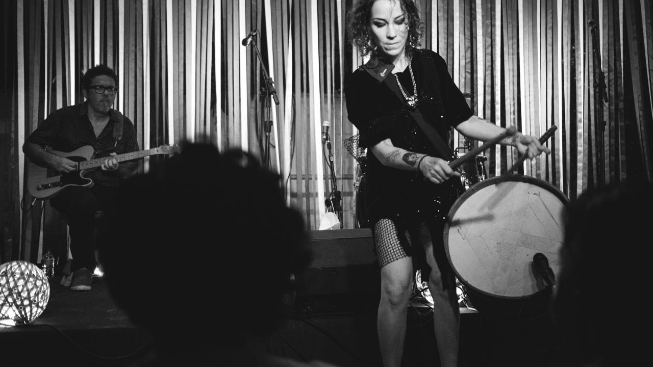 Imagem em preto e branco mostra mulher tocando tambor em cima de palco