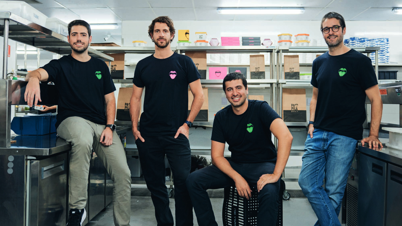 Quatro homens brancos de camiseta preta da Papila Deli em cozinha industrial.