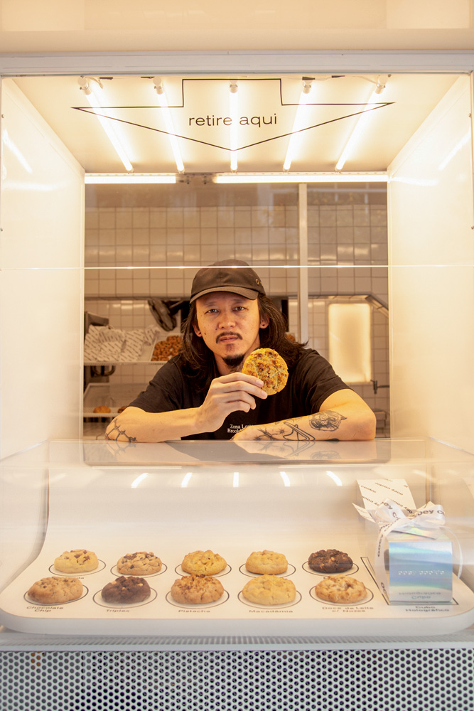 Homem asiático segurando cookie na mão atrás de vitrine de vidro de cookies.