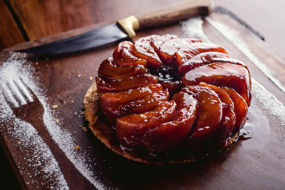 Tarte tatin com gomos caramelados de maçã sobre tampo de madeira.