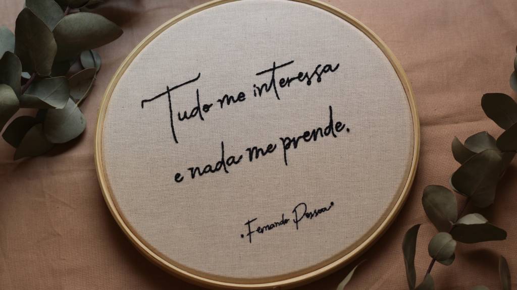 Tecido bordado com parte de poema de Fernando Pessoa.