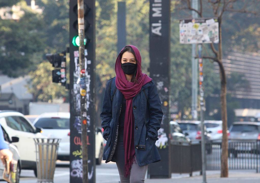 Mulher caminha de máscara e cachecol enrolado no pescoço e na cabeça na Avenida Paulista