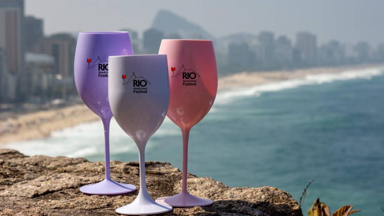 Três taças de vinho de plástico sobre pedras em frente à orla de Copacabana no Rio de Janeiro.