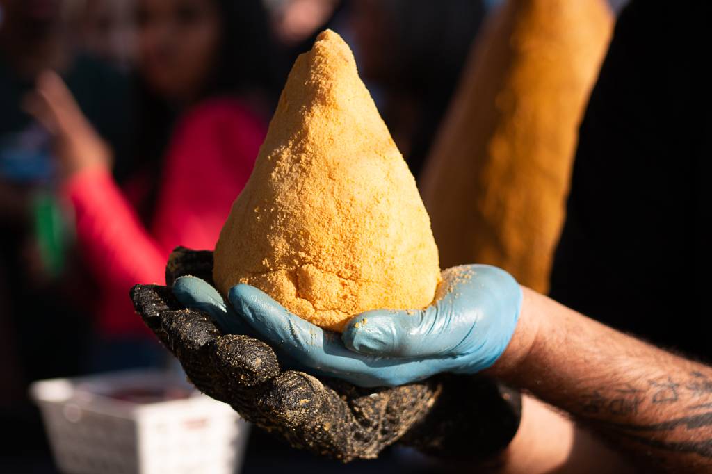 Mãos com luvas seguram uma coxinha gigante.